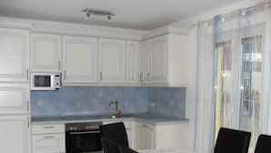 A kitchen with white cabinets, a microwave, an oven, and a dining table with chairs. - Villa Lake Constance View (Stetten)