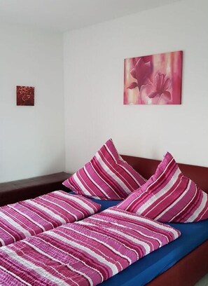 A bed with striped bedding and a single pillow, a small framed artwork on the wall, and a dark bench against the wall. - Villa Lake Constance View (Stetten)