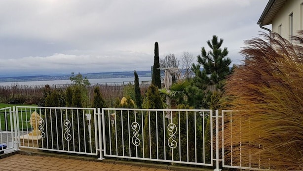 A patio with a brick floor, white decorative fence, and a view of a body of water and trees in the background. - Villa Lake Constance View (Stetten)