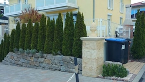 A yellow building with a balcony, stone wall, and a trash bin. - Villa Lake Constance View (Stetten)