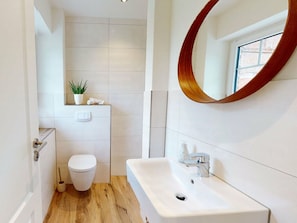 A modern bathroom with a toilet, sink, and a mirror with a wooden frame. - Holiday Home Small Island (Fehmarn)