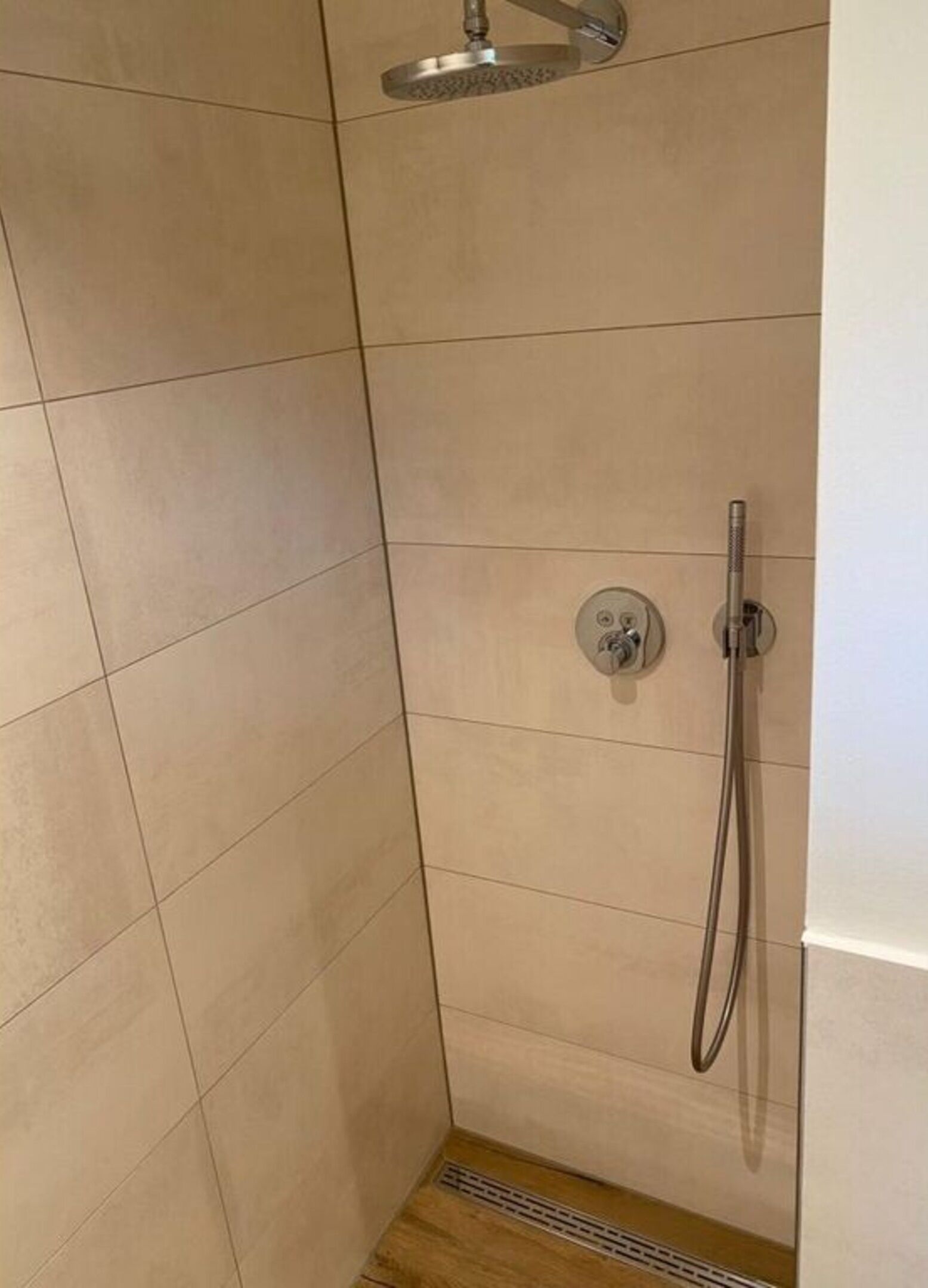 A corner shower with beige tiles, a handheld showerhead, and a wall-mounted control panel.