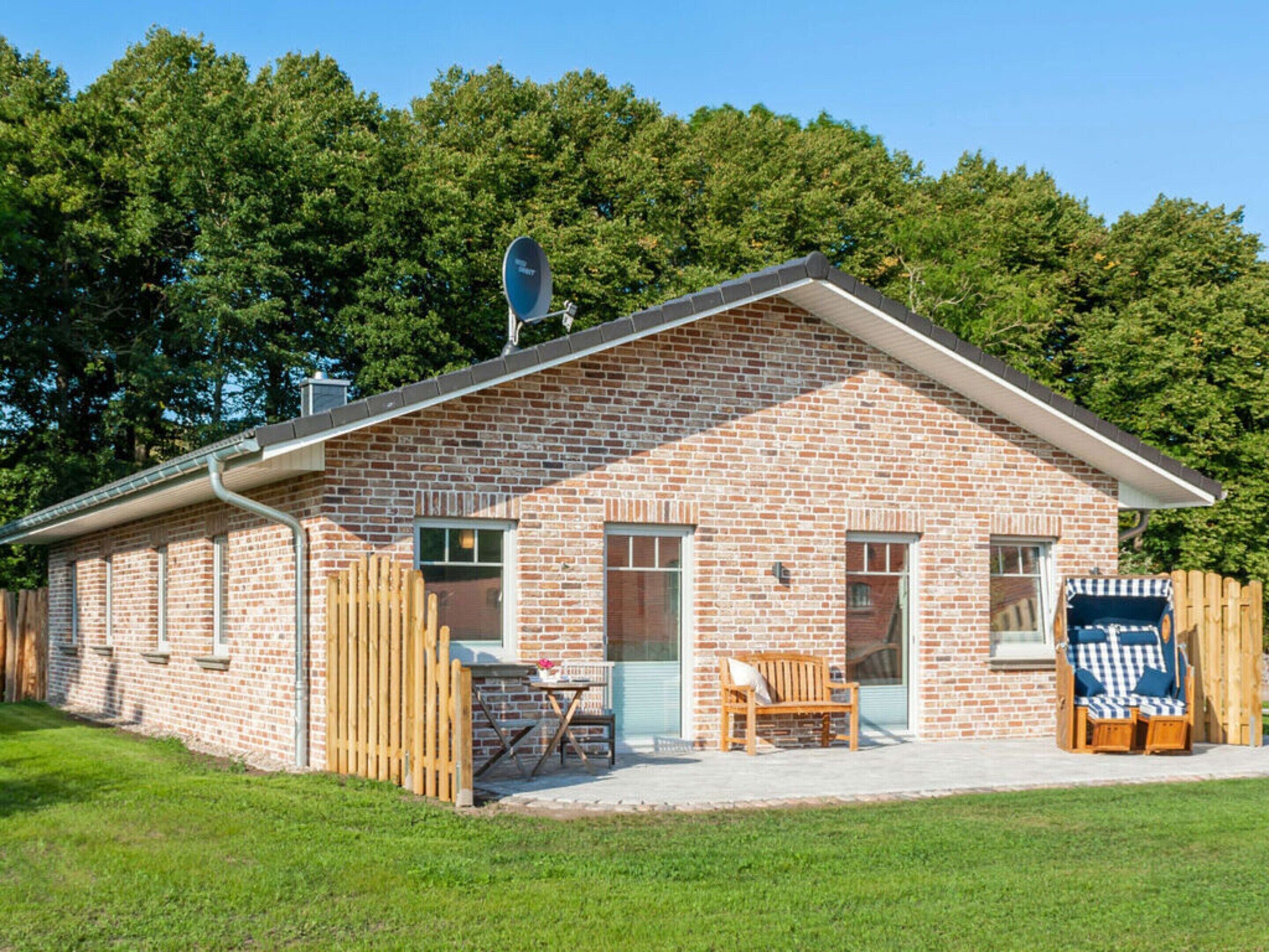 A brick building with a sloped roof, a satellite dish, and a fenced yard with a bench and a chair.