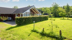 Ett hus med ett sluttande tak, en täckt uteplats och en välskött gräsmatta.
