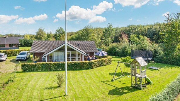 En bostadsfastighet med en välskött gräsmatta, ett trähus som används som lekstuga och ett hus med ett tak täckt av takpannor.