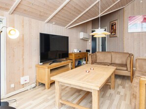 A living room with a television, wooden furniture, and a ceiling with exposed beams.