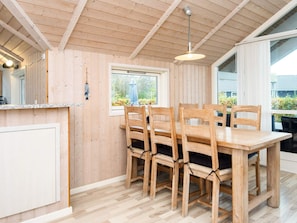 Un interior de madera con una mesa de comedor y sillas, una lámpara colgante y una ventana con vistas a la vegetación.