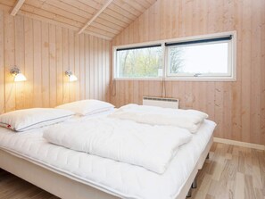 A bedroom with a wooden ceiling, a bed with white bedding, two wall-mounted lamps, and a window with a view of trees. - 4 Star Holiday Home in Sydals (Sydals)