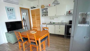 Une cuisine compacte comprenant une table à manger, des chaises, un réfrigérateur et un téléviseur.