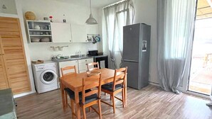 Une cuisine compacte comprenant un lave-linge, une table à manger avec des chaises, un réfrigérateur et une fenêtre avec des rideaux.