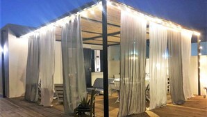 Un espace extérieur abrité, doté d’une terrasse en bois, comprenant un coin salon et une petite table.