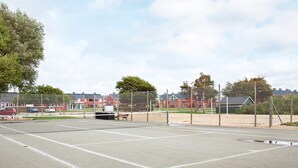 Un court de tennis avec un filet, entouré d’une clôture et d’arbres.