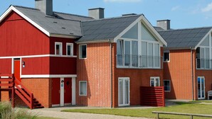 Une rangée d’immeubles aux façades en briques rouges, dotés d’un design moderne, de grandes fenêtres et d’un toit plat.