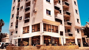 Un hotel de varios pisos con fachada plana, balcones y un restaurante en la planta baja.