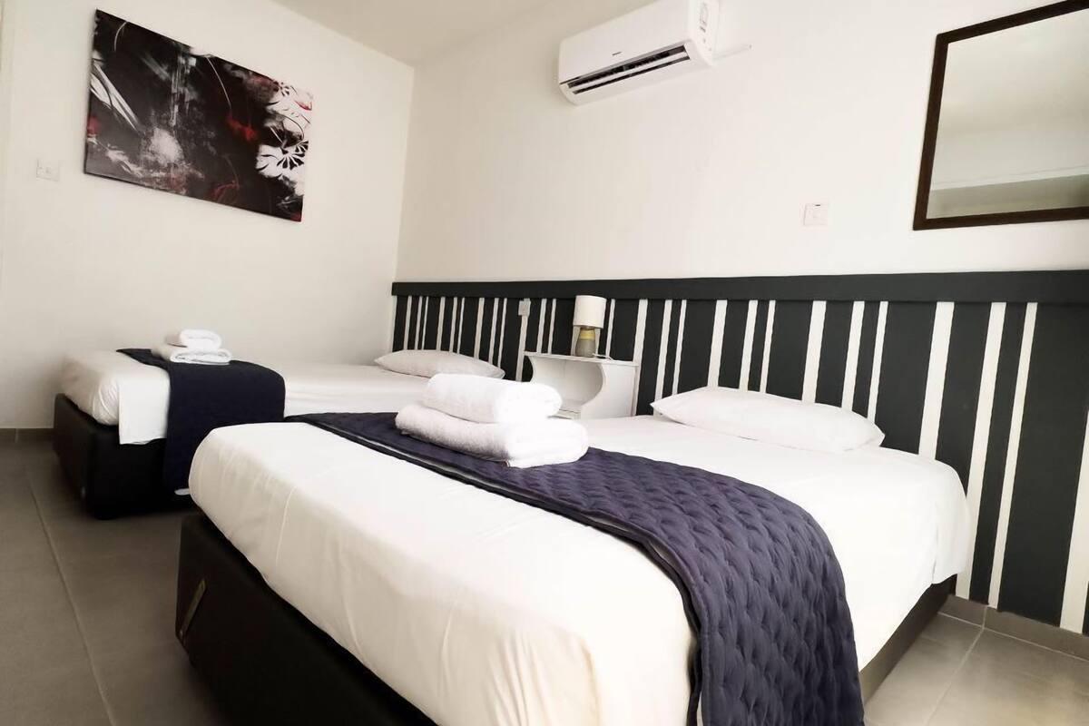 Una habitación de hotel moderna con una cama grande, una mesita de noche, un equipo de aire acondicionado y un espejo fijado a la pared.