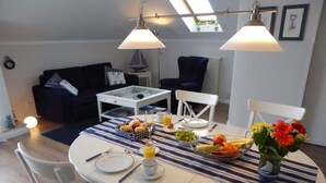 Un comedor con una mesa redonda dispuesta para el desayuno, con diversas frutas y un jarrón de flores.