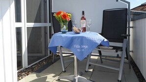 Un patio al aire libre con una mesa preparada para dos personas, una botella de vino y un jarrón con flores.