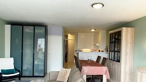 Een woonkamer met een bank, een eettafel met stoelen en een keuken met kastjes.
