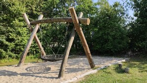 A wooden swing set with a tire swing, surrounded by sand and grass, with trees in the background. - 4 Person Holiday Home in Hemmet (Hemmet)