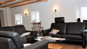 A modern living room with leather sofas, a glass coffee table, and wooden beams on the ceiling. - Eifel Farmhouse Comfortable Holiday Residence (Plütscheid)