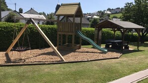 A playground with a swing set, slide, and small wooden playhouse. - Eifel Farmhouse Comfortable Holiday Residence (Plütscheid)