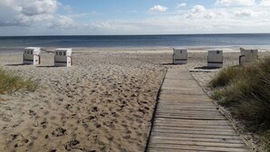 Una pasarela de madera que lleva a cabañas de playa numeradas 102 y 103 en una playa arenosa bajo un cielo despejado.