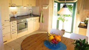 Una cocina con armarios de madera, una estufa y un lavamanos. Hay un frutero sobre la mesa y una planta en la esquina.