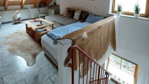 A spacious loft with a high ceiling, a wooden staircase, a sofa, a coffee table, and a view of the outdoors. - Alpennest Comfortable Holiday Residence (Fuessen)