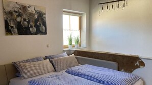 A bedroom with a bed, checkered bedding, a window with plants, and a cowhide wall accent. - Alpennest Comfortable Holiday Residence (Fuessen)