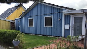 A blue single-story house with a small front yard, a paved driveway, and a door with a window. - Schwedenhaus am Kai 14i (Grossenbrode)