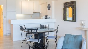 Een moderne keuken met witte kastjes, een centraal eiland met zitplaatsen en een eettafel met stoelen.