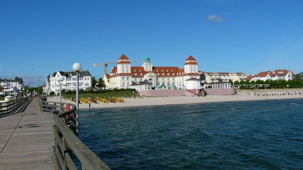 A waterfront promenade with a wooden walkway, a large building with red roofs, and a beach area. - Modern Apartment Near Seabeach (Binz)