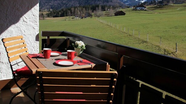 A balcony with a table set for two, overlooking a mountainous landscape. - Hochgrat View in Steibis, Haus Akelei (Oberstaufen)