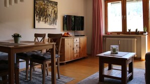 A cozy living room with a wooden dining table, chairs, a TV, and a painting on the wall. - Hochgrat View in Steibis, Haus Akelei (Oberstaufen)