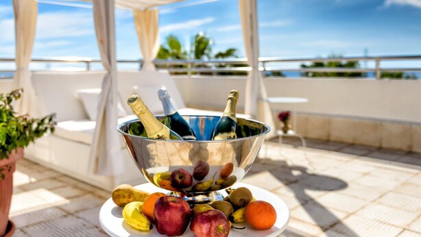 Una mesa con frutero y botellas de champán en una terraza con vistas al mar.