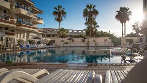 Una piscina con sillas de descanso, palmeras y un edificio con balcones.