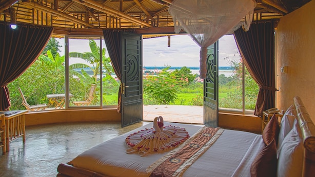 A room with a bed, a view of greenery and water outside, and a mosquito net over the bed. - Hanchey Bamboo Resort  (Stueng Trang)