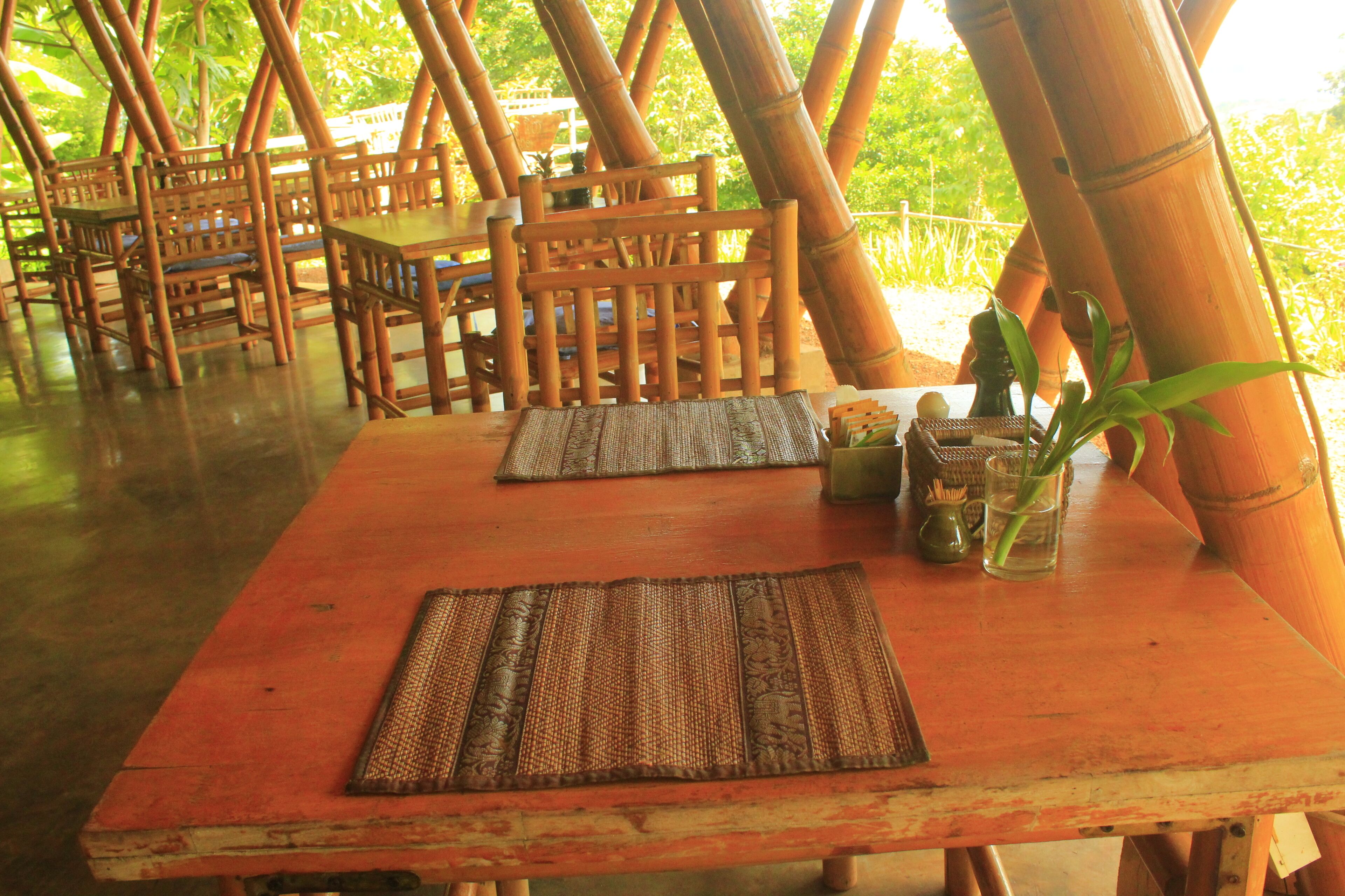 A dining area with bamboo chairs and tables, some with placemats.