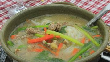 Un tazón de sopa con fideos, carne y verduras sobre una mesa con mantel a cuadros.
