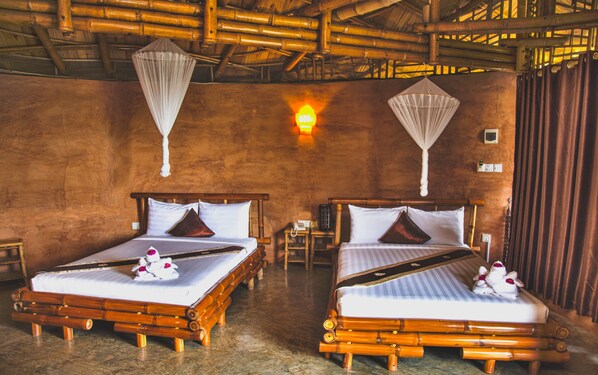 Two wooden beds with white linens and decorative pillows, a wall-mounted light, and a bamboo ceiling.