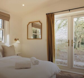 Une chambre à coucher avec un lit, une lampe de chevet, un miroir et une porte-fenêtre coulissante donnant sur un jardin.