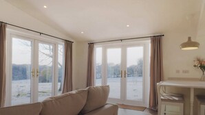 A spacious living room with a beige sofa, a dining table with chairs, and large sliding glass doors leading to a view of a snowy landscape.