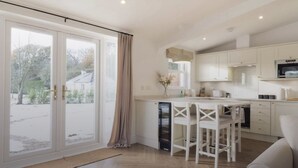 A modern kitchen with white cabinetry, a dining area with white chairs, and a large sliding glass door leading to a garden.