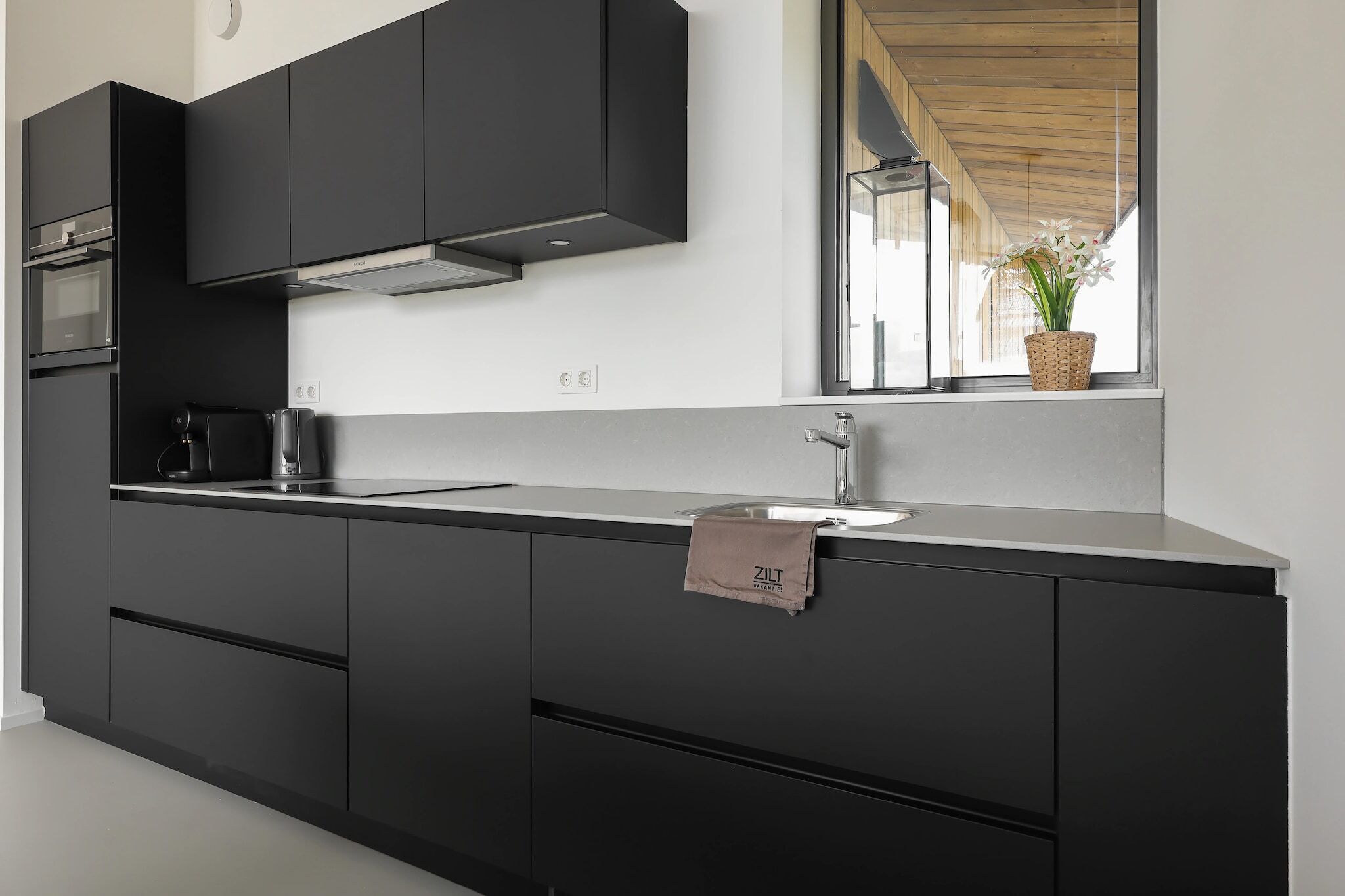 Een moderne keuken met donkere kastjes, een roestvrijstalen spoelbak en een raam met uitzicht op de omgeving.