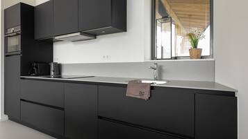 Een moderne keuken met donkere kastjes, een roestvrijstalen spoelbak en een raam met uitzicht op de omgeving.