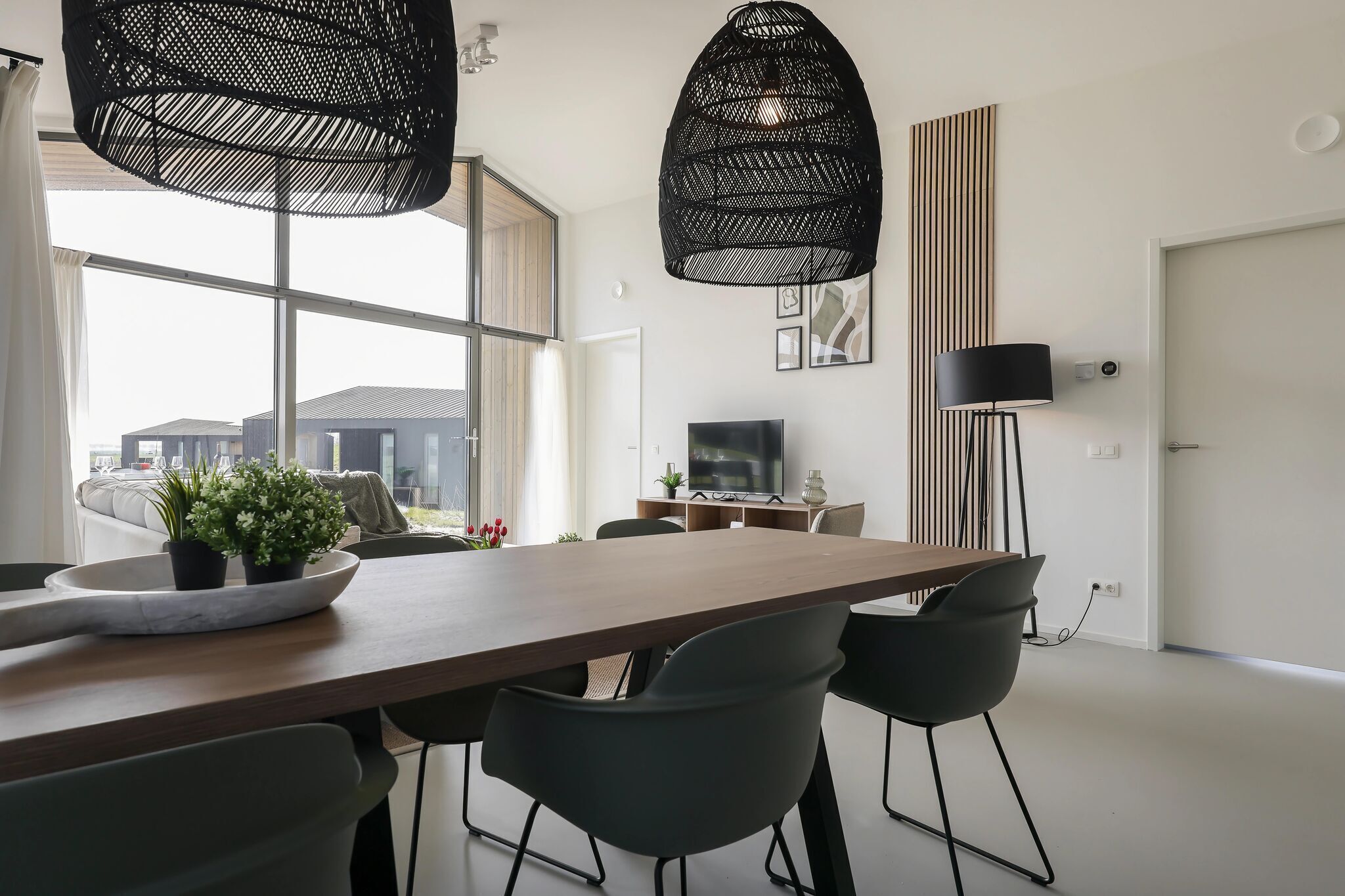 Un espace repas moderne avec une table en bois, des chaises noires et deux lampes suspendues noires.