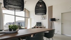 Uma zona de refeições moderna com uma mesa de madeira, cadeiras pretas e duas luminárias pendentes pretas.