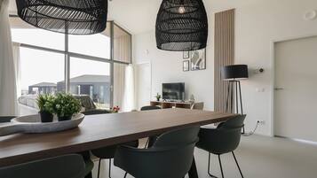 Un espace repas moderne avec une table en bois, des chaises noires et deux lampes suspendues noires.