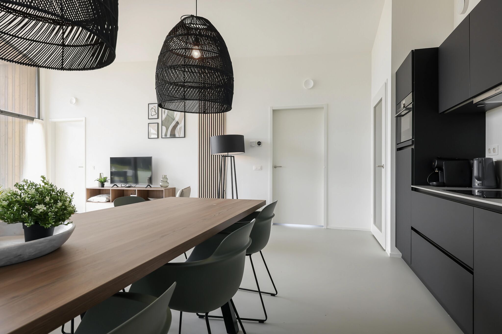 Een moderne keuken met zwarte kastjes, een houten eettafel en twee hanglampen.