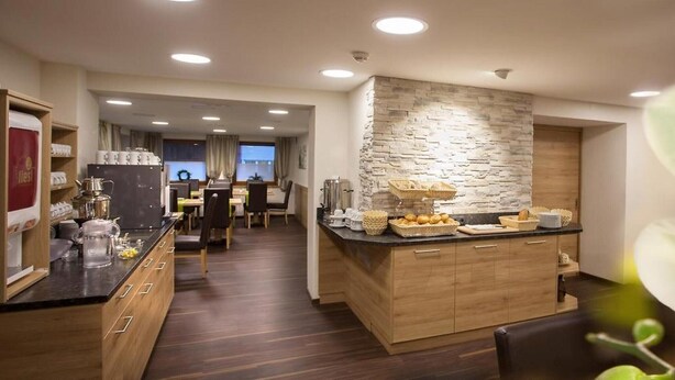 A modern kitchen with a stone accent wall, wooden cabinets, and a breakfast bar. - Property in Langenfeld (Laengenfeld)